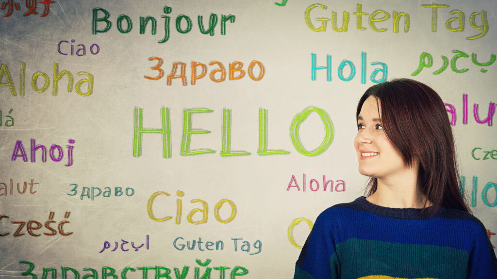 woman smiling in front of a board covered in the word "hello" in many different languages and colors