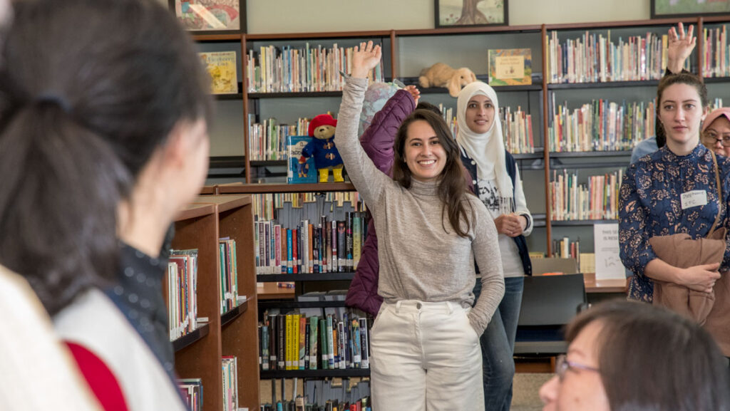 A group of international teachers at the UNCG School of Education smile and raise their hands