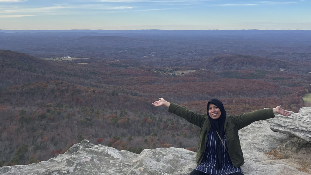 Baiq Desy Ratnasari poses on an overlook with her arms outstretched