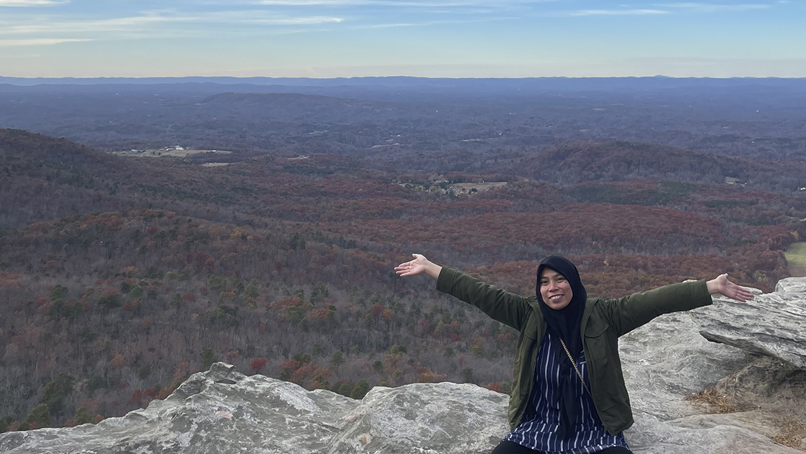 Baiq Desy Ratnasari in Indonesia, standing on a mountain side with her arms stretched out.